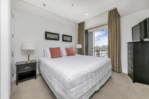 a white bedroom with a large bed and a television at Sun Soaked Corner Apartment with Harbour View in Auckland +66 photos
