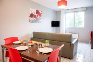 a dining room table with red chairs and a couch at Comfort Aparthotel Besancon La City in Besançon