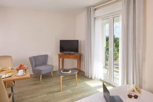 a living room with a television and a table with a chair at Quality Aparthotel Portes de Rennes in Bruz