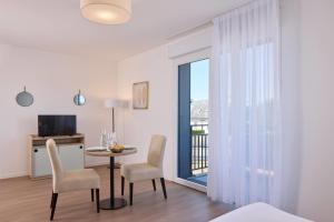 a living room with a table and chairs and a window at Quality Aparthotel Ploërmel in Ploërmel