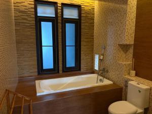 a bathroom with a tub and a toilet and windows at Villa Tara Khaolak in Khao Lak