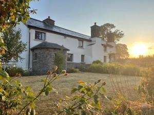 a large white house with the sun setting behind it at 16th Century Devon Farmhouse Stunning Views in Winkleigh