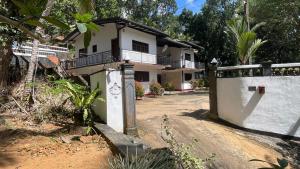 a white house with a fence next to a dirt road at Reefside mount villa in Deniyaya