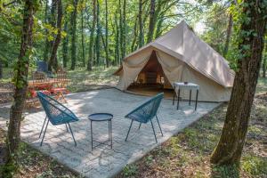 a tent with chairs and a table in the woods at La Permaculturelle - Domaine des Ramières in Le Poët-Laval