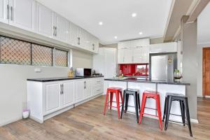a kitchen with white cabinets and red stools at Coal d' Vine Chillout - Cessnock NSW in Cessnock