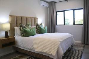 a bedroom with a large white bed with green pillows at Lhondeh Apartments in Livingstone