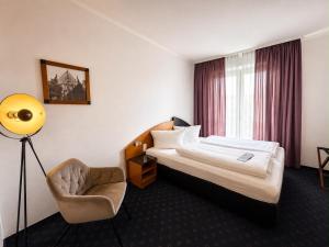 a hotel room with a bed and a chair at Hotel Belmondo Leipzig Airport by Mayburgh in Wiedemar