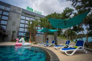 a pool with chairs and umbrellas next to a building at ibis Styles Batam Nagoya in Nagoya