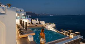 a woman standing next to a swimming pool on a house at La Perla Villas and Suites - Adults Only in Oia