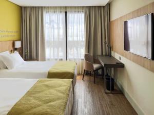 a hotel room with two beds and a desk and a television at Mercure Itajai Navegantes in Itajaí