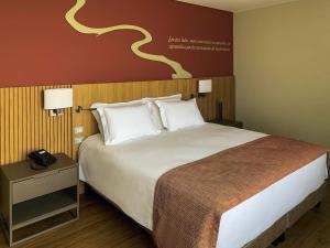 a bed in a hotel room with a phone on a table at Mercure Itajai Navegantes in Itajaí