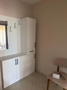 a kitchen with white cabinets and a chair and a window at Kodra Apartament in Golem