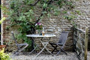 a table and two chairs in front of a stone wall at Finest Retreats - The Little Barn in Great Somerford