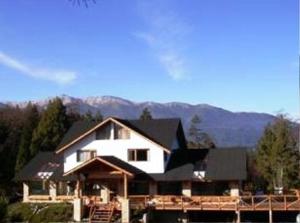 una grande casa bianca con montagne sullo sfondo di Apart Hotel y Hosteria del Sir a Villa La Angostura