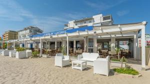 a building with white chairs and tables on the beach at Hotel Kennedy in Lido di Savio