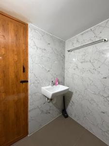 a white bathroom with a sink and a wooden door at Suraksha Homestay in Malpe