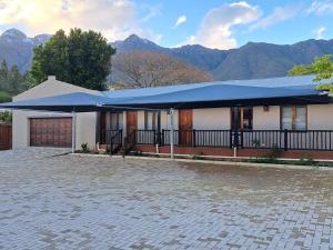 a house with a blue roof with mountains in the background at Grace Walk Guest House in Swellendam