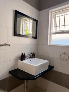 ein weißes Waschbecken in einem Badezimmer mit Spiegel in der Unterkunft Langholm Hotel in Walvis Bay