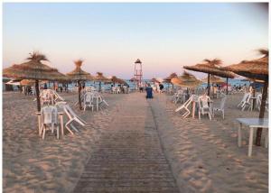 a sandy beach with chairs and umbrellas and tables at دار المحبة - Dar El Mahabba in Tazarka