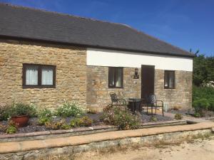 a stone house with chairs and a table in front of it at Bakers Mill Holiday Cottages in Beaminster