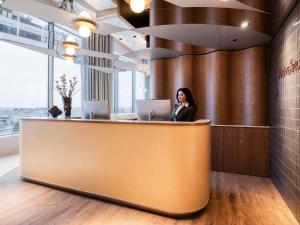 a woman sitting at a counter in an office with two laptops at Mövenpick Hotel Brussels Airport in Zaventem