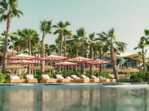 a resort pool with chairs and umbrellas and palm trees at SLS The Red Sea in Ḩanak