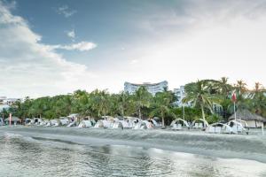 a beach with white chairs and palm trees and buildings at Decameron Galeon - All Inclusive in Santa Marta