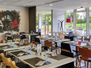 a dining room with tables and chairs and windows at Novotel Saclay in Saclay