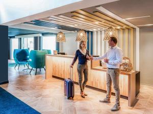 a man and woman shaking hands in a hotel lobby at Novotel Lens Noyelles in Noyelles-Godault +172 photos