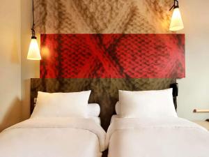 two white beds in a room with a red wall at ibis Senlis in Senlis