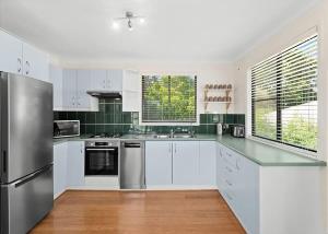 a kitchen with white cabinets and a stainless steel refrigerator at Mindil Arch Walk to 3 Beaches & River in Tomakin