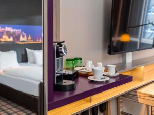 a room with a bed and a tv and cups on a table at Mercure Salzburg City in Salzburg