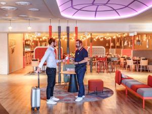 two men standing in a restaurant with their luggage at Hôtel Mercure Lille Aéroport in Lesquin