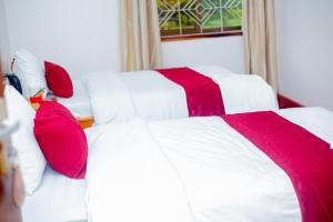 two white beds with red pillows in a bedroom at Furavia Hotel stay in Moshi