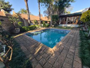 a swimming pool in a yard with a brick sidewalk at Ambiance Guesthouse in Pretoria
