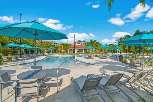 a pool with tables and chairs and blue umbrellas at Vista Cay Luxury Loft in Orlando
