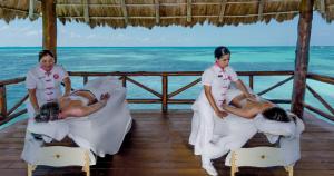 two women performing a massage on beds in front of the ocean at Mia Reef Isla Mujeres - All Inclusive Resort in Isla Mujeres