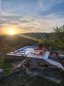 a pool with benches and the sunset in the background at Cabañas Dulce Atardecer in Villa Carlos Paz
