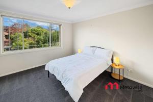 a white bedroom with a bed and a window at Spacious 4-Bedroom Home in Cherrybrook in Cherrybrook