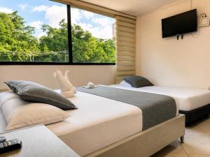 two beds in a bedroom with a tv on the wall at Hotel Laureles Palo Alto in Medellín