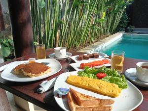 a table with plates of breakfast food and a pool at Sri Abi Ratu Villa in Sukawati