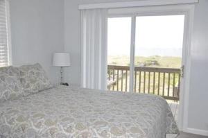 a bedroom with a bed with a view of a balcony at Dune Deck South - Duplex in Holden Beach
