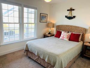 a bedroom with a bed with red pillows and two windows at Compass Rose in Holden Beach