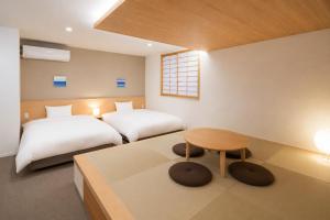 a bedroom with two beds and a table and a window at NAGI Hiroshima Hotel and Lounge in Hiroshima
