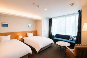 a hotel room with two beds and a couch at NAGI Hiroshima Hotel and Lounge in Hiroshima