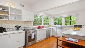 a white kitchen with white cabinets and a table at King Parrot Cottage - Close To Beach in Pearl Beach