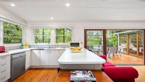 a kitchen with white cabinets and a table with a bowl of fruit at King Parrot Cottage - Close To Beach in Pearl Beach