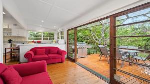 a living room with a red couch and a table at King Parrot Cottage - Close To Beach in Pearl Beach