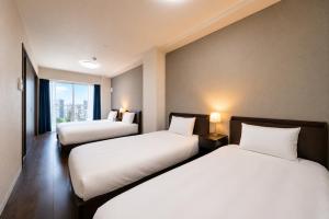 two beds in a room with a window at Hotel Piacere NAMBA in Osaka