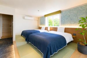 two blue and white beds in a room with a potted plant at Nagi Kurashiki Hotel&Lounge in Kurashiki